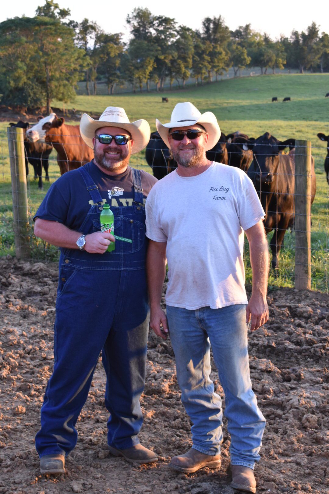 Two men in cowboy hats smiling with cows in the background.
