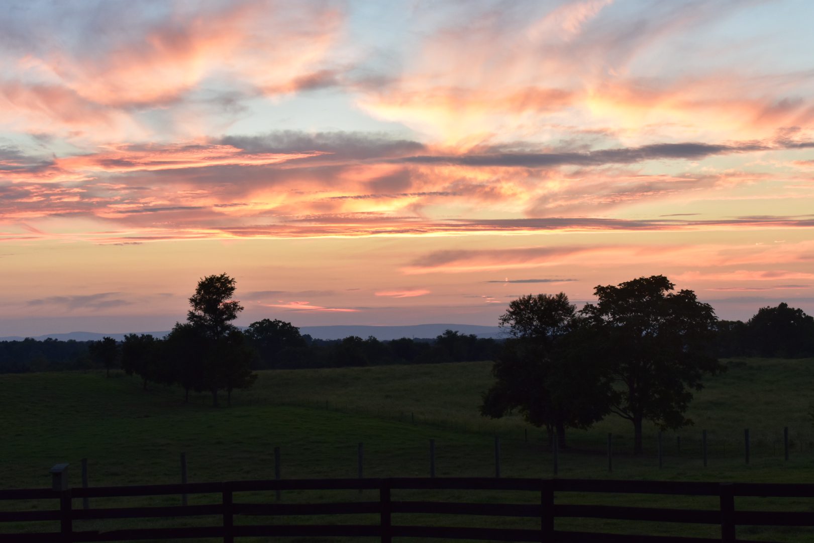 Colorful sunset over a peaceful countryside landscape with trees and fences.