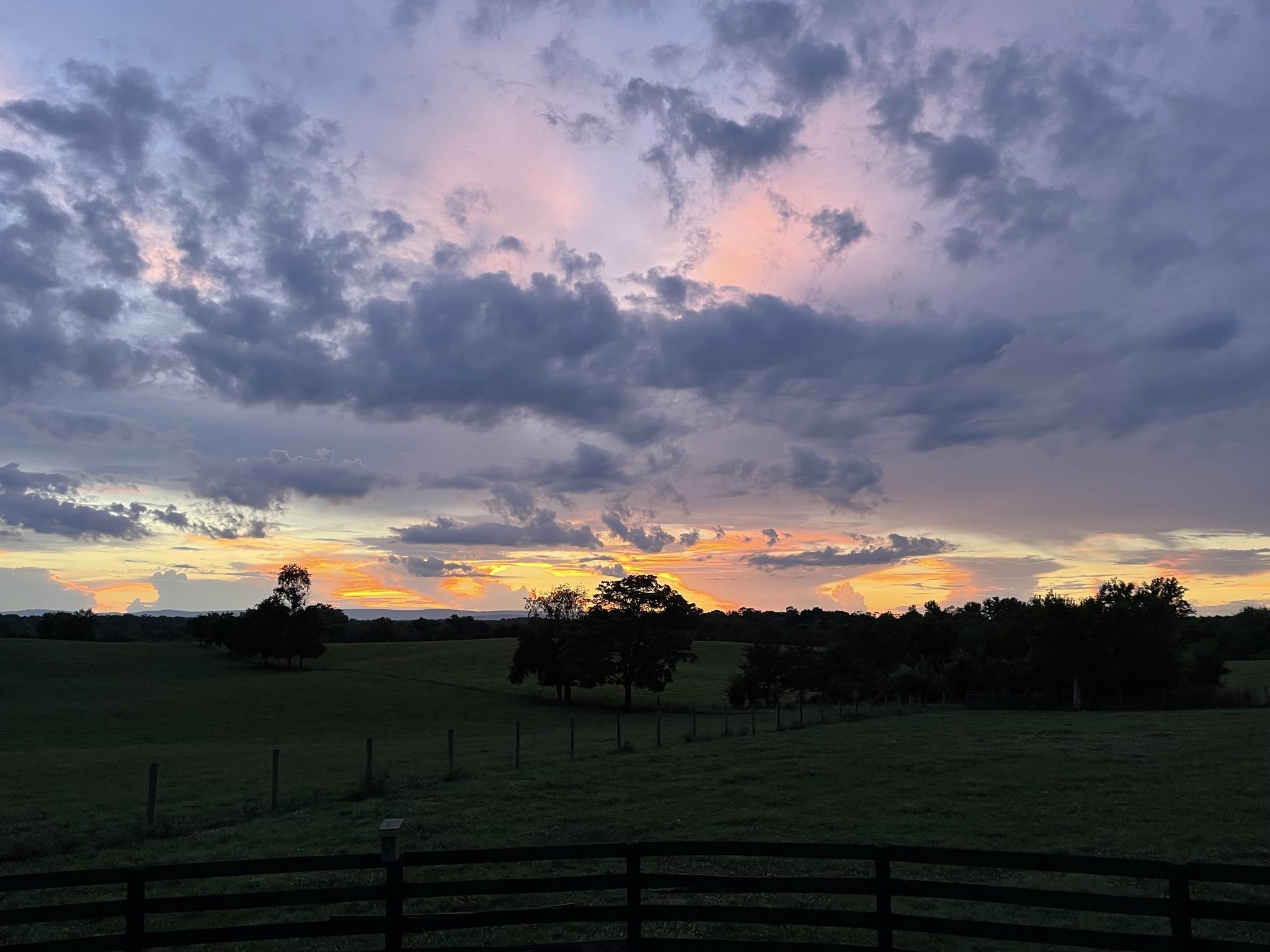 A vibrant sunset with dramatic clouds over a fenced field.