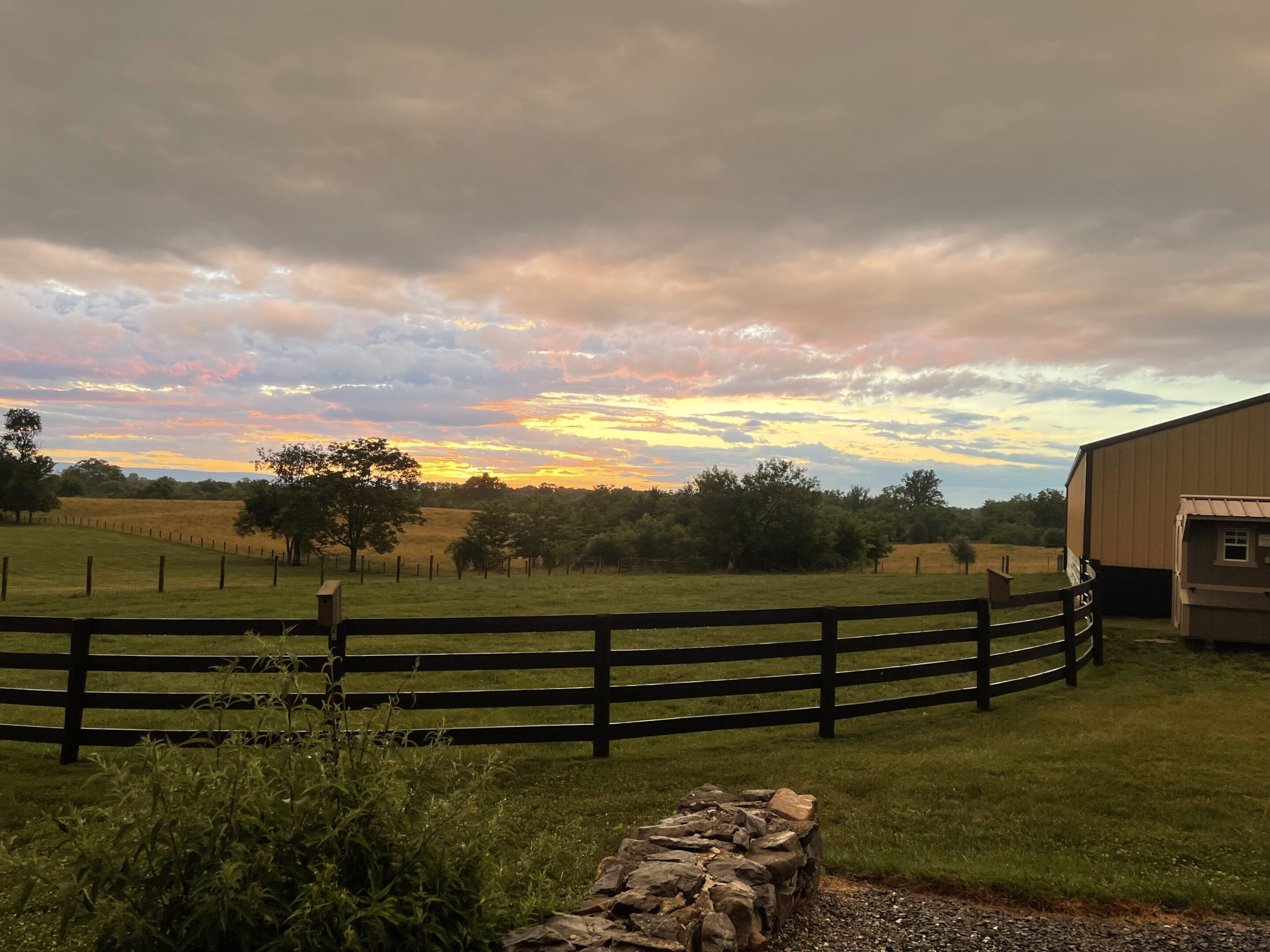 Sunset over a peaceful countryside with a wooden fence and open fields.